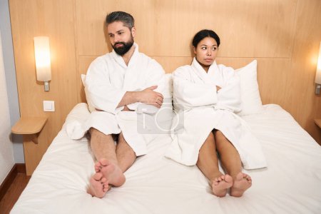 Photo for Low-spirited man and his despondent female companion seated in bed looking in different directions - Royalty Free Image