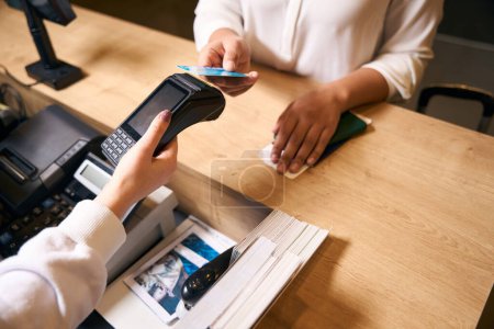 Photo for Cropped photo of woman touching her payment card against POS terminal in female receptionist hand - Royalty Free Image