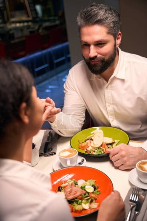 Téléchargez les photos : Jeune homme sérieux tenant sa compagne à la main à la table du restaurant - en image libre de droit