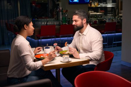 Photo for Serious young man and his happy female companion eating at restaurant table - Royalty Free Image