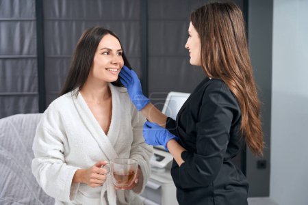Photo for Doctor in blue gloves and protective suit touching patient face, preparing for procedure - Royalty Free Image