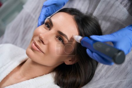 Doctor in protective gloves holding device and doing post acne treatment in salon
