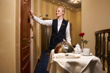 Camarera agradable llamando a la puerta de la habitación del hotel, ella entregó la comida para una cena romántica