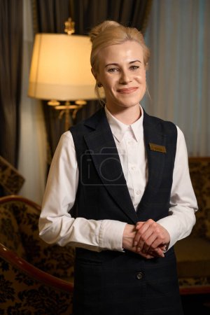 Photo for Young woman administrator stands in a room with a luxurious interior, in the background a floor lamp - Royalty Free Image
