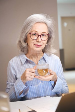 Foto de Sofisticada dama se estableció con una taza de té y un ordenador portátil en la mesa de la cocina - Imagen libre de derechos