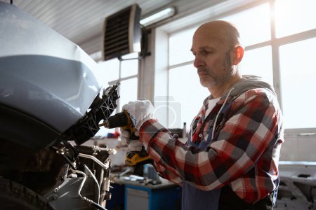 Téléchargez les photos : Spécialiste de la réparation automobile travaille avec une voiture dans un atelier de voiture, il porte des gants de protection - en image libre de droit