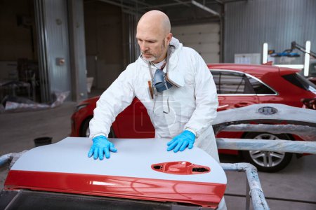 Photo pour Homme d'âge moyen sur le lieu de travail est engagé dans la réparation automobile, en arrière-plan est une voiture rouge - image libre de droit