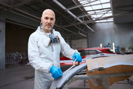 Photo for Painter prepares a part of the car body for work, the man is in a large car repair shop - Royalty Free Image