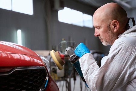 Photo for Man in a repair shop at the stage of polishing the stripped sections of red car, man uses special tool - Royalty Free Image