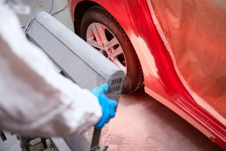 Téléchargez les photos : Réparateur utilise séchage infrarouge des endroits apprêtés, dans l'atelier dans la réparation d'une voiture rouge - en image libre de droit