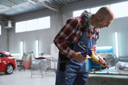 Foto de Maestro masculino en el taller de reparación utiliza pegamento especial, un hombre con ropa de trabajo - Imagen libre de derechos