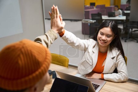Photo for Pleased female office worker seated at laptop giving high five to coworker - Royalty Free Image