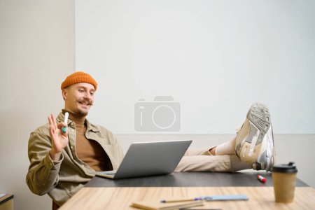 Photo for Cheerful young corporate manager seated at desk with marker in hand looking at laptop screen - Royalty Free Image