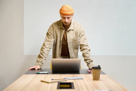 Téléchargez les photos : Travailleur de bureau concentré sérieux appuyé sur le bureau et regardant l'écran d'ordinateur portable dans la salle de réunion - en image libre de droit