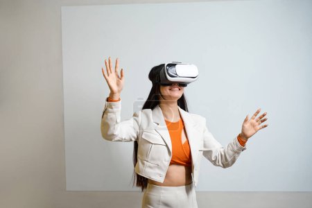 Photo for Smiling contented female employee in VR headset standing against wall with whiteboard - Royalty Free Image