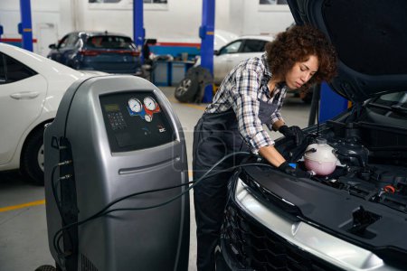 Photo pour Femme mécanicien automobile vérifie un climatiseur de voiture, elle utilise un système spécial de rinçage pour le climatiseur - image libre de droit