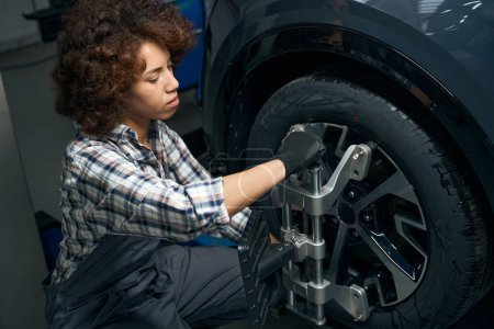 Foto de Mujer mecánico automático realiza el equilibrio de la rueda, ajusta la alineación de la rueda, una mujer en mono de trabajo - Imagen libre de derechos