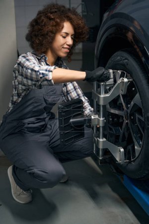 Foto de Joven mecánico automático realiza el equilibrio de la rueda, ajusta la alineación de la rueda, capataz en mono de trabajo - Imagen libre de derechos
