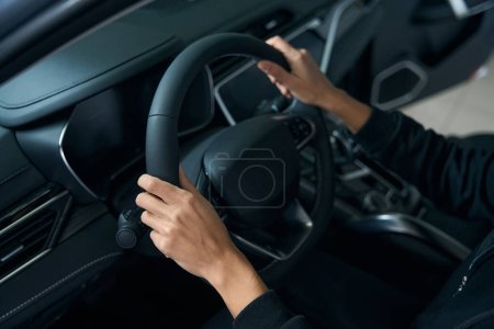 Photo for Hands of a young woman lie on the steering wheel of a modern car, interior is made in dark colors - Royalty Free Image
