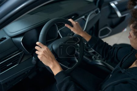 Foto de Mujer de pelo rizado se sienta detrás del volante en el interior de un coche moderno, sus manos yacen en el volante - Imagen libre de derechos