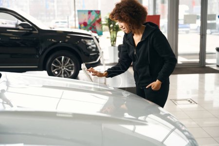 Photo for Smiling car dealership client choosing a new car, woman in comfortable casual clothes - Royalty Free Image