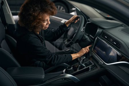 Téléchargez les photos : Jeune femme conducteur assis derrière le volant à l'intérieur d'une voiture moderne, la femme appuie sur le bouton de démarrage - en image libre de droit
