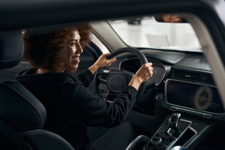 Photo for Smiling multiracial driver sits behind the wheel in the interior of a modern car, woman in comfortable clothes - Royalty Free Image