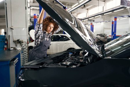 Téléchargez les photos : Employé d'un atelier de réparation automobile ouvre le capot d'une voiture, la voiture est en cours d'entretien - en image libre de droit