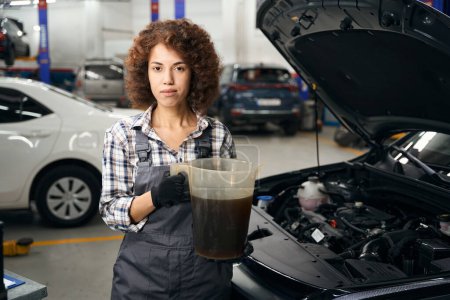 Téléchargez les photos : Femme réparateur spécialiste change d'huile dans une voiture, une femme travaille dans un atelier de réparation automobile moderne - en image libre de droit