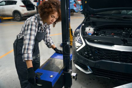 Foto de Joven multirracial femenina utiliza equipo especial para inspeccionar un coche, una mujer trabaja en un taller de reparación de automóviles moderno - Imagen libre de derechos