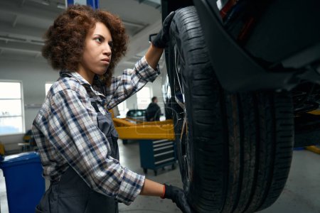 Foto de El coche está siendo atendido en un taller de reparación de automóviles moderno, una mujer reparador inspecciona una rueda de coche - Imagen libre de derechos