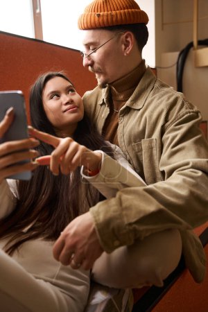 Téléchargez les photos : Aimer gars étreignant sa jeune femme heureuse souriante avec smartphone à la main - en image libre de droit