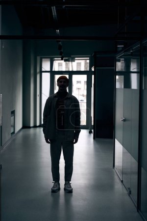 Téléchargez les photos : Portrait grandeur nature d'un homme caucasien adulte souriant debout seul dans un couloir sombre - en image libre de droit