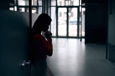 Foto de Vista lateral de una joven empleada deprimida apoyada contra la pared - Imagen libre de derechos