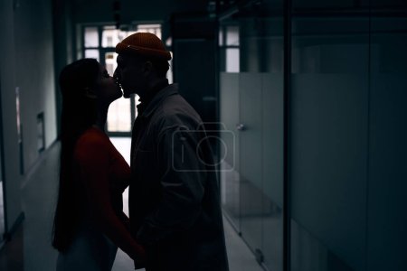 Photo for Side view of young man and woman kissing on lips in dark corridor - Royalty Free Image