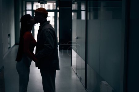 Foto de Vista lateral de un joven macho besándose hembra en los labios en corredor oscuro - Imagen libre de derechos