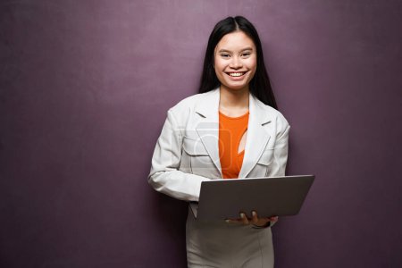 Photo for Smiling happy elegant lady with laptop in hands standing against wall and looking before her - Royalty Free Image