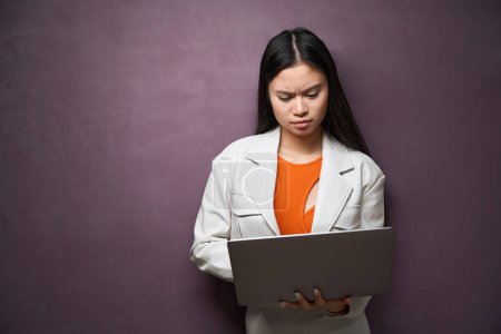 Photo for Waist-up portrait of serious focused woman typing on portable computer while standing by wall - Royalty Free Image