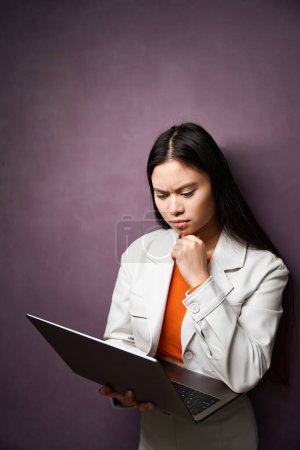 Téléchargez les photos : Femme concentrée lisant quelque chose sur ordinateur portable dans ses mains tout en se tenant par le mur - en image libre de droit