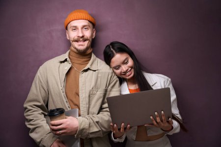 Téléchargez les photos : Portrait taille haute de femme souriante et homme heureux avec des ordinateurs portables debout au mur - en image libre de droit