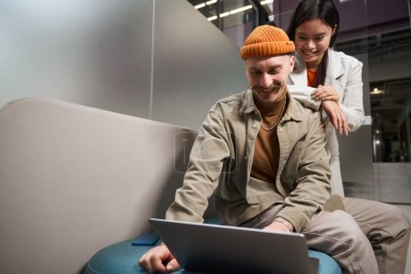 Téléchargez les photos : Sourire gars heureux en utilisant un ordinateur portable en présence de sa compagne - en image libre de droit