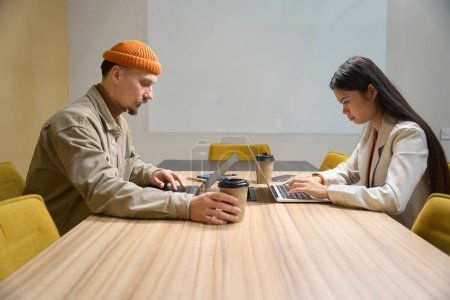 Foto de Empleados serios de la empresa sentados en el escritorio escribiendo en sus computadoras portátiles - Imagen libre de derechos
