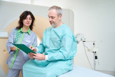 Téléchargez les photos : Patient masculin signant un questionnaire avant diagnostic CT en laboratoire - en image libre de droit