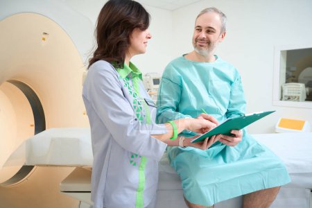 Téléchargez les photos : Heureux homme adulte tenant questionnaire avant diagnostic IRM en laboratoire - en image libre de droit