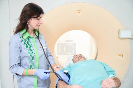 Foto de Médico sonriente midiendo la presión arterial del paciente masculino con tonómetro antes del diagnóstico por RM - Imagen libre de derechos