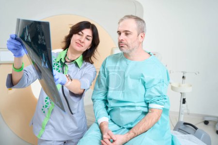 Téléchargez les photos : Médecin féminin et patient masculin sont à la recherche d'images IRM en clinique - en image libre de droit