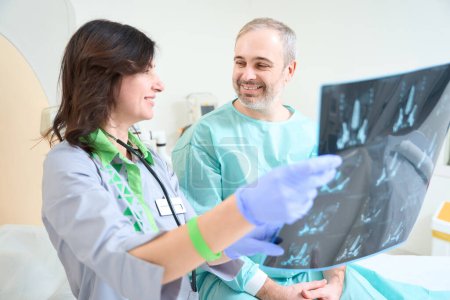 Foto de Feliz doctor en guantes con imágenes de resonancia magnética en la clínica mientras se la muestra al paciente - Imagen libre de derechos