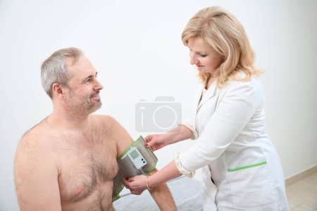 Téléchargez les photos : Médecin souriant appliquant un dispositif de moniteur holter sur la main de l'homme à l'hôpital - en image libre de droit