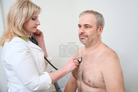 Photo for Doctor using stethoscope, checking up heart beat in doctor office at hospital. Medical and health care concept - Royalty Free Image