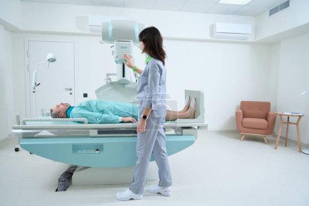 Foto de Mujer joven médico radiólogo configurar la máquina para tomar paciente de rayos X - Imagen libre de derechos